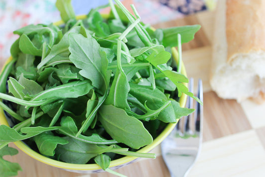 kale and spinach leaves in a bowl and a knife and bread in the background