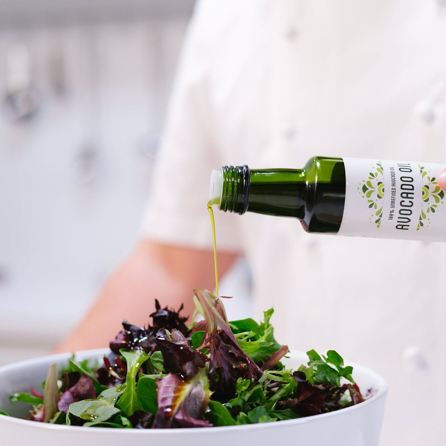 Bottle of Avocado oil being poured onto a bowl of mixed greens