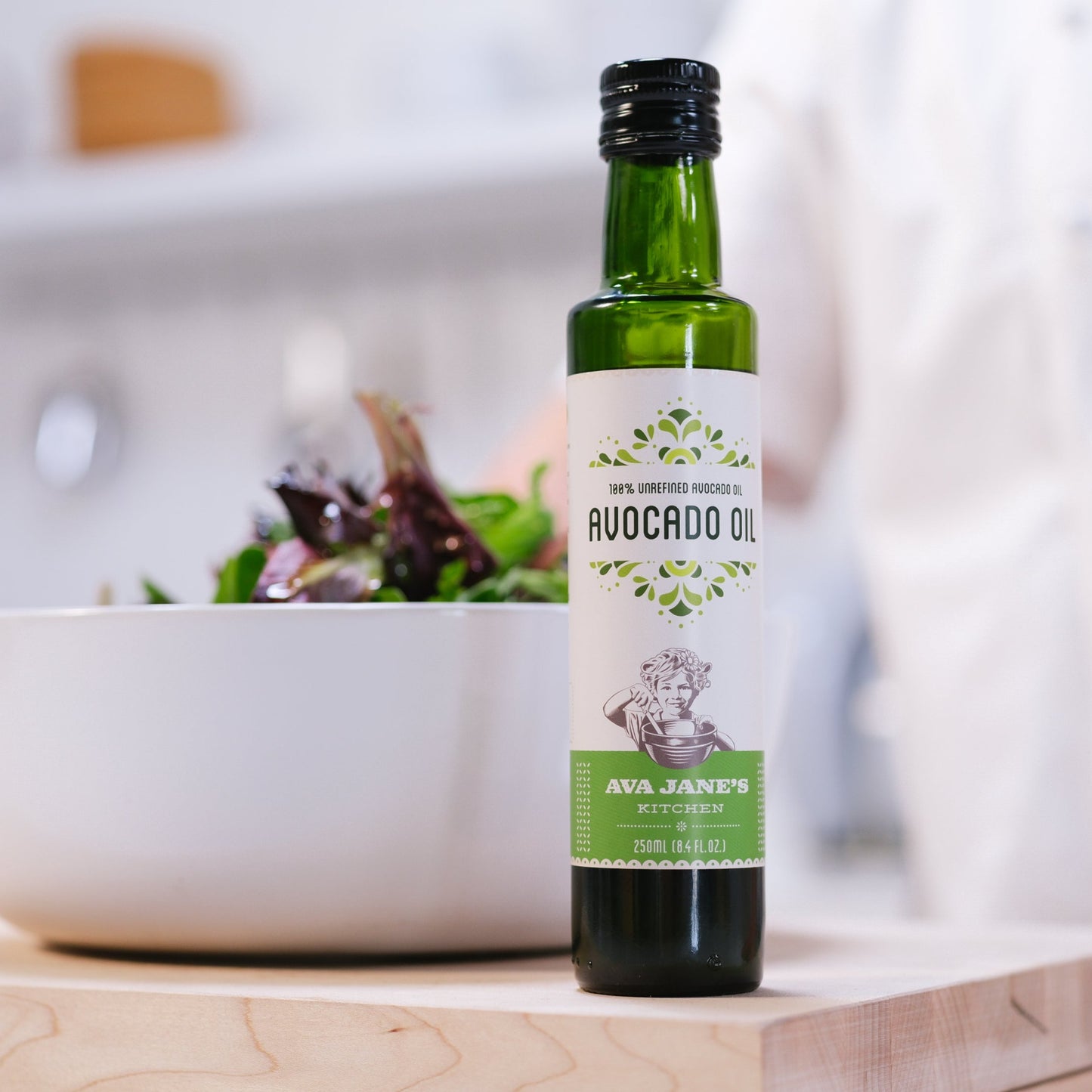 Bottle of Ava Jane's Kitchen's Avocado Oil sitting on a cutting board in front of a big white bowl of salad