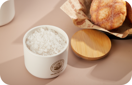 an open air tight salt cellar containing sea salt and a wooden lid placed on a smooth surface