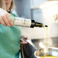 Photo of a woman pouring avocado oil into a stainless steel skillet